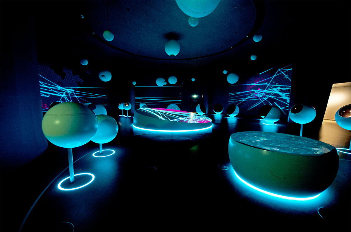 A dark room with blue lights from the floor lighting up various cosmology innstallations.