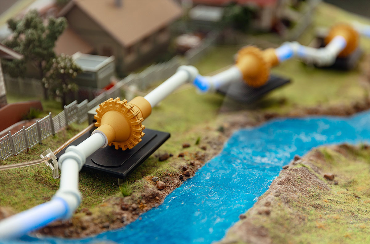 A model of water pipes on the ground alongside a river.