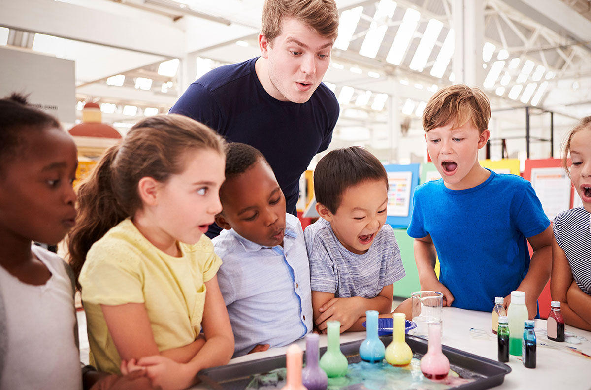 Male teacher standing with pupils watching a science experiment.