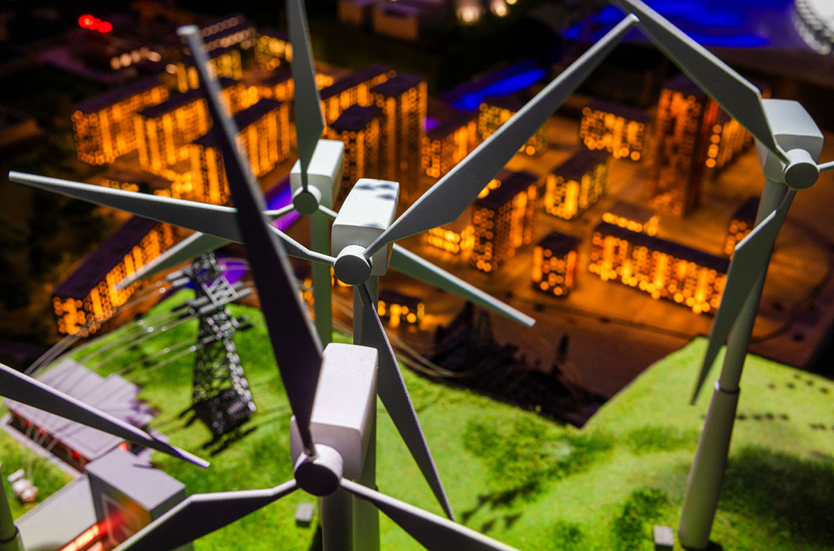 A model of multiple wind turbines in front of lit up city buildings.